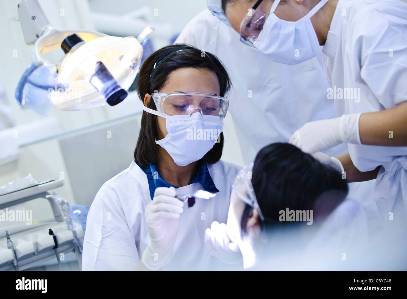 Studenti di odontoiatria bianco da indossare maschere chirurgiche occhiali e tuniche in ambiente clinico di eseguire un intervento di chirurgia dentale su paziente Foto Stock