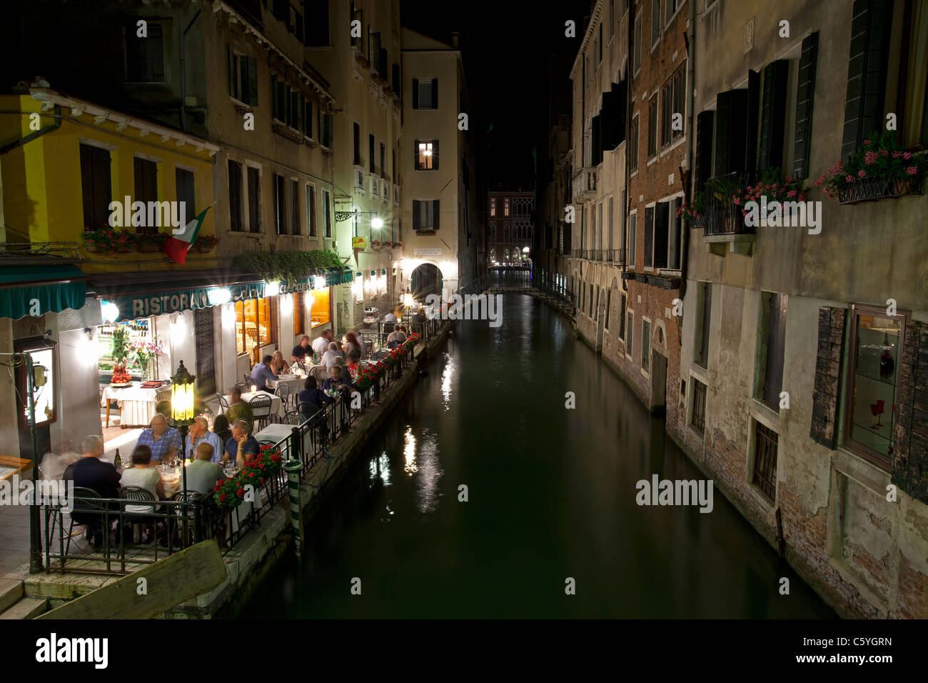 Venezia, Italia di notte, una piccola caffetteria, ristorante, su uno stretto canale con persone sedute lungo il bordo delle acque e romantiche luci Foto Stock