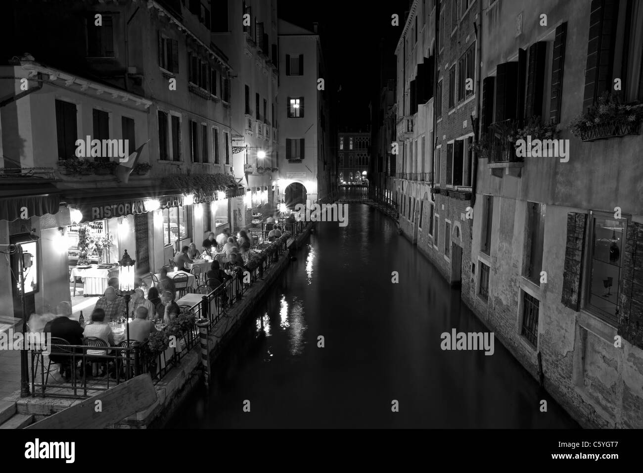 Venezia, Italia di notte, una piccola caffetteria, ristorante, su uno stretto canale con persone sedute lungo il bordo delle acque e romantiche luci Foto Stock