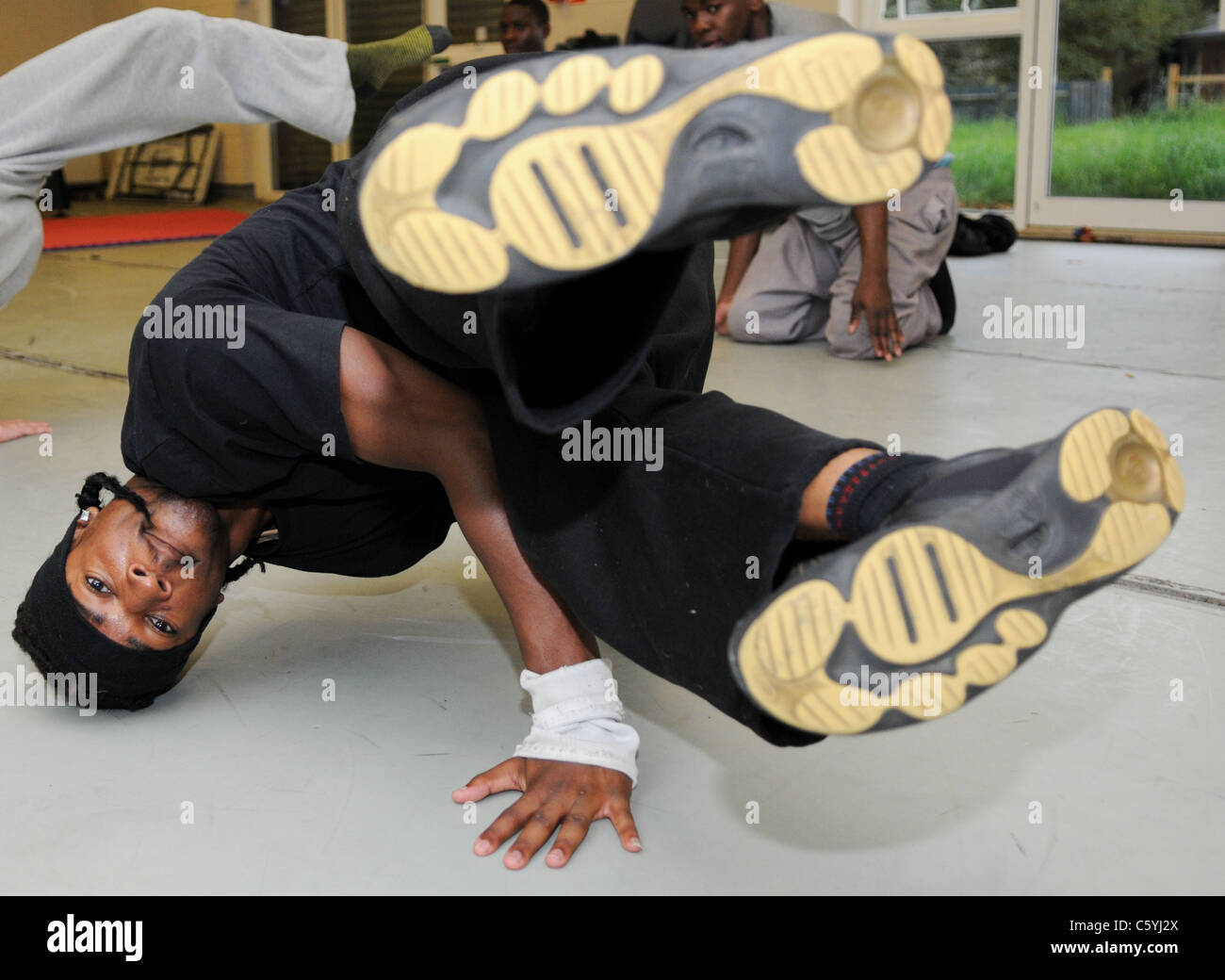 Nero giovani adolescenti in una danza di strada di filatura di classe sulla sua testa con il suo trainer in aria concentrandosi sul suo break dance Foto Stock