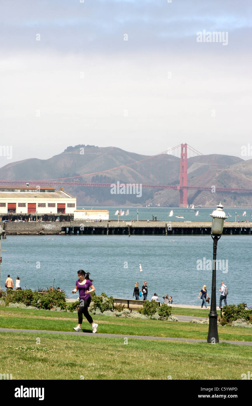Pedoni godendo di San Francisco Maritime National Historical Park con il Ponte Golden Gate e la baia in background Foto Stock