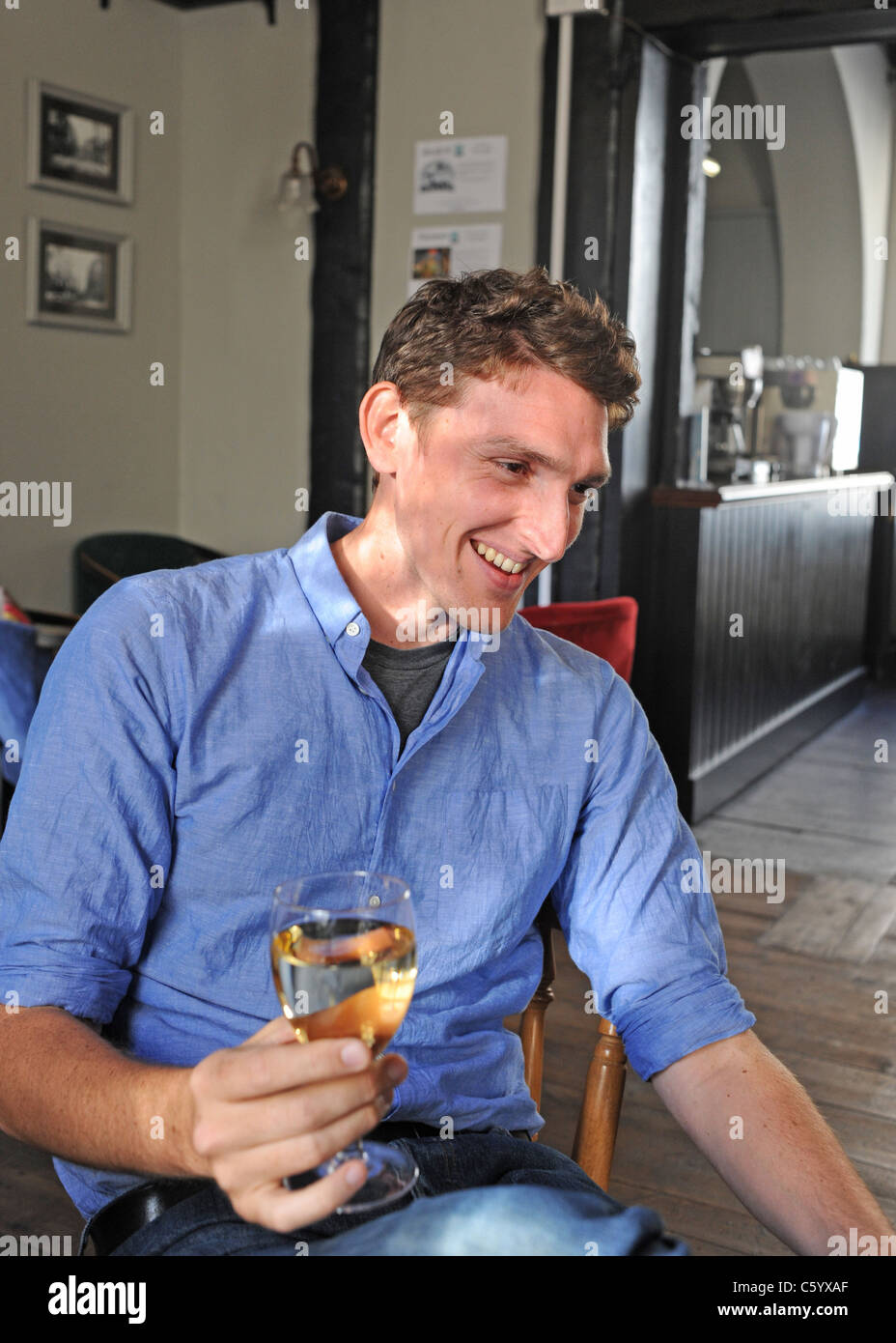 Giovane uomo in British pub bevendo un grande bicchiere di vino bianco Foto Stock