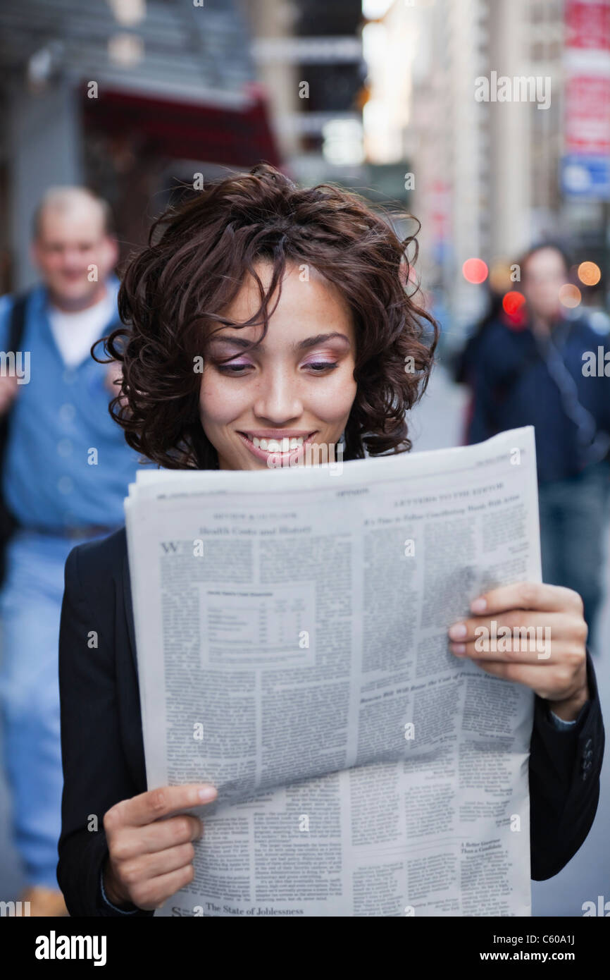 Stati Uniti d'America, New York New York City, sorridente imprenditrice la lettura di giornale su strada Foto Stock