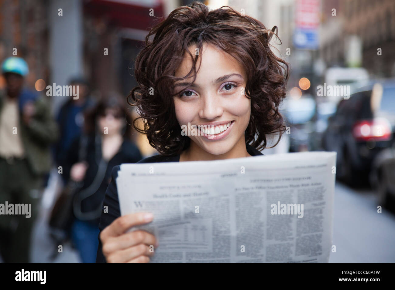Stati Uniti d'America, New York New York City, ritratto di donna sorridente azienda giornale su strada Foto Stock