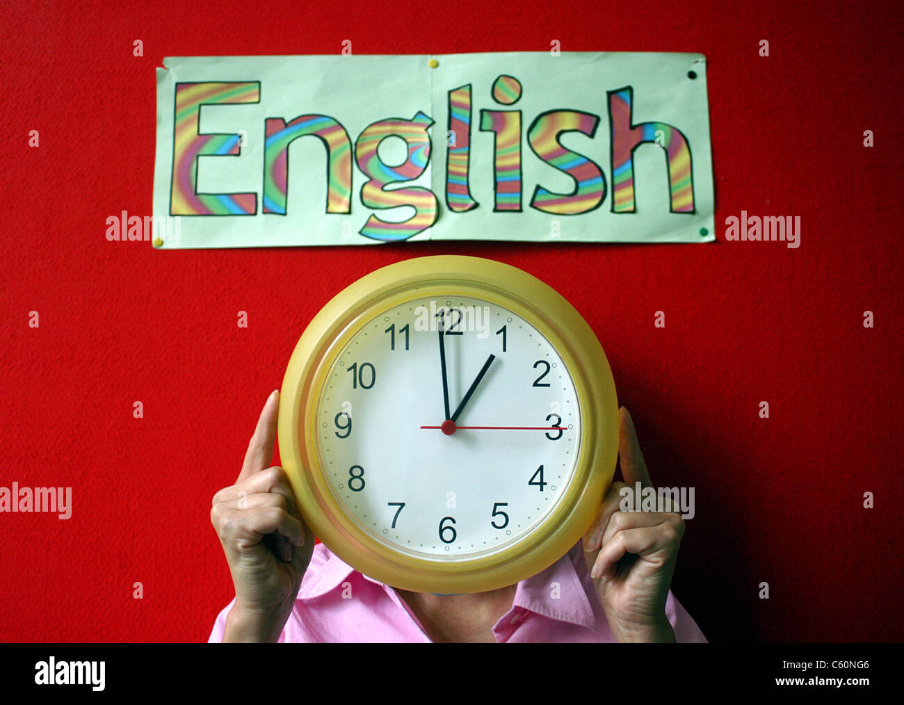 Adulto tenendo in mano un orologio giallo, stette in piedi contro un muro rosso con un poster artwork dicendo inglese, in multi-lettere colorate Foto Stock