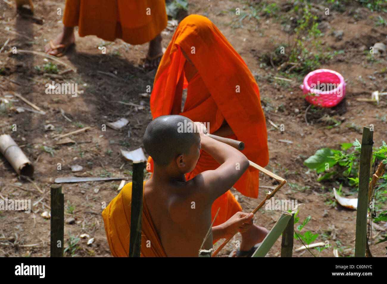 Tre giovani buddisti bonzes lavorando in un orto il taglio di legno per la realizzazione di una copertura a Luang Prabang, Laos Asia Foto Stock
