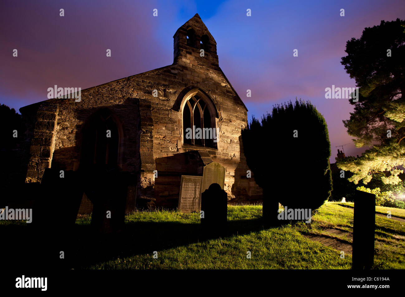 L'esterno e il cimitero di una piccola chiesa duecentesca di notte. Foto Stock