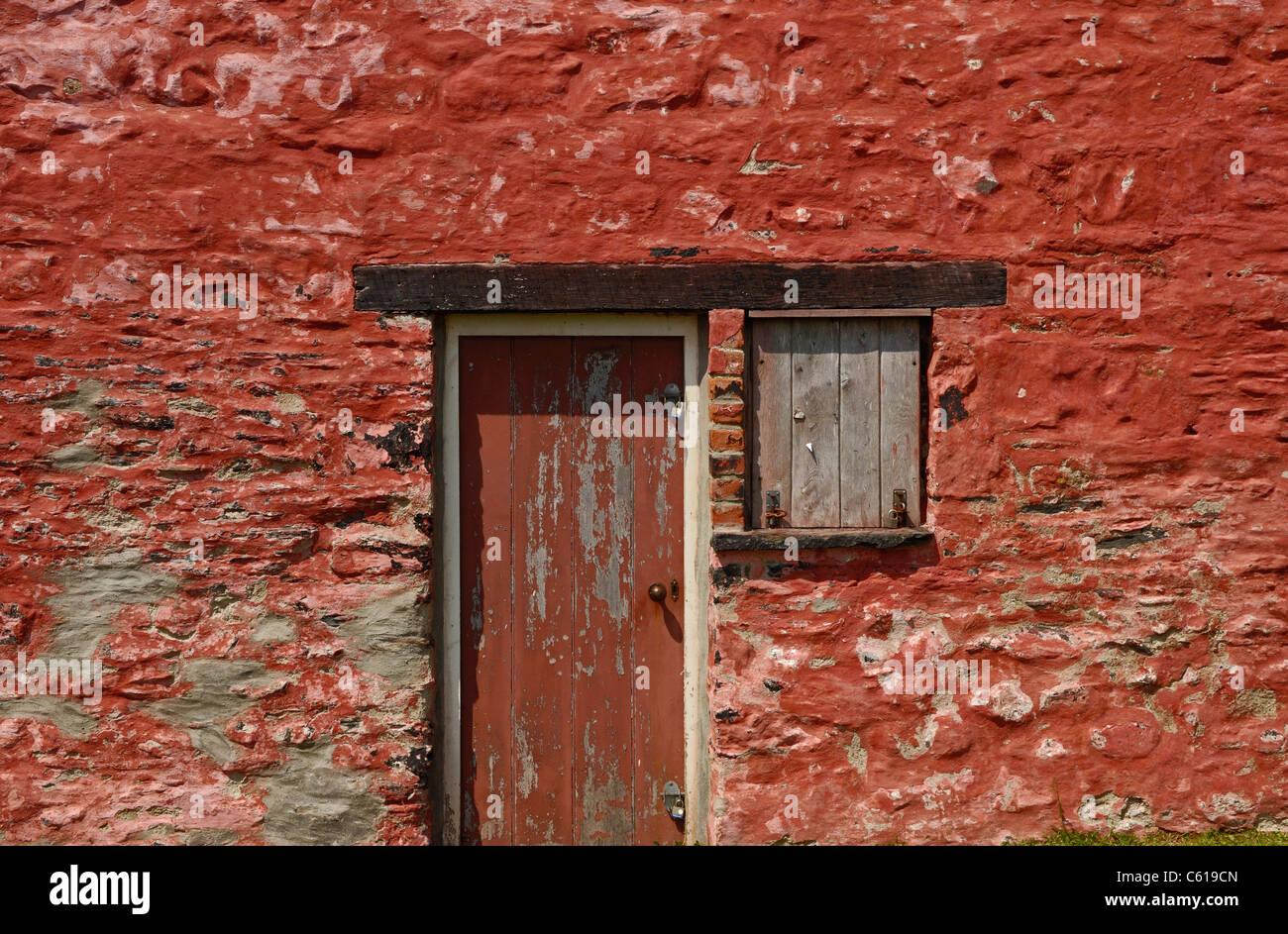 Edificio di pietra o store dipinte di rosso con porta di legno e di un otturatore in legno per una finestra Foto Stock