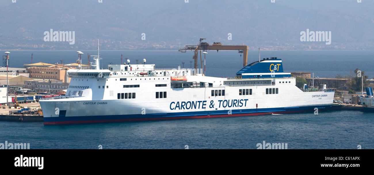 Una nave traghetto lascia la città portuale di Messina, Sicilia con il porto industriale in background, mostrando il Mare Mediterraneo Foto Stock