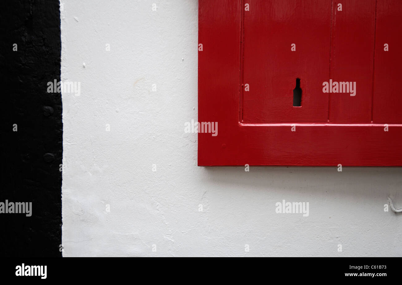 Dipinto di rosso nella finestra in legno otturatore contro un bianco parete dipinta e un nero del telaio della porta. Foto Stock