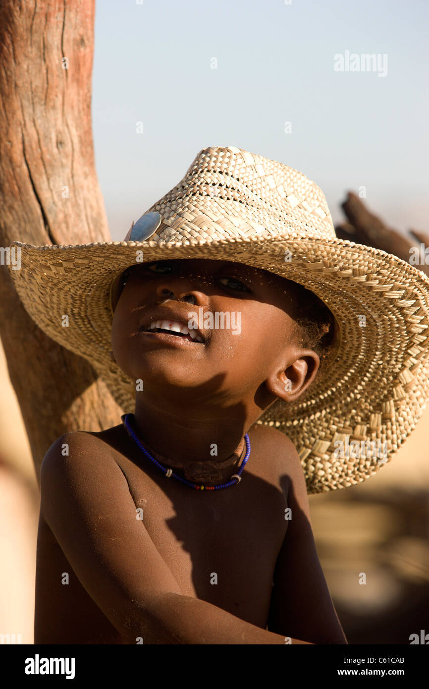 Un giovane ragazzo Himba gioca con un grande cappello di paglia. Purros, Northern Kaokoland, Kaokoveld, Namibia. Foto Stock