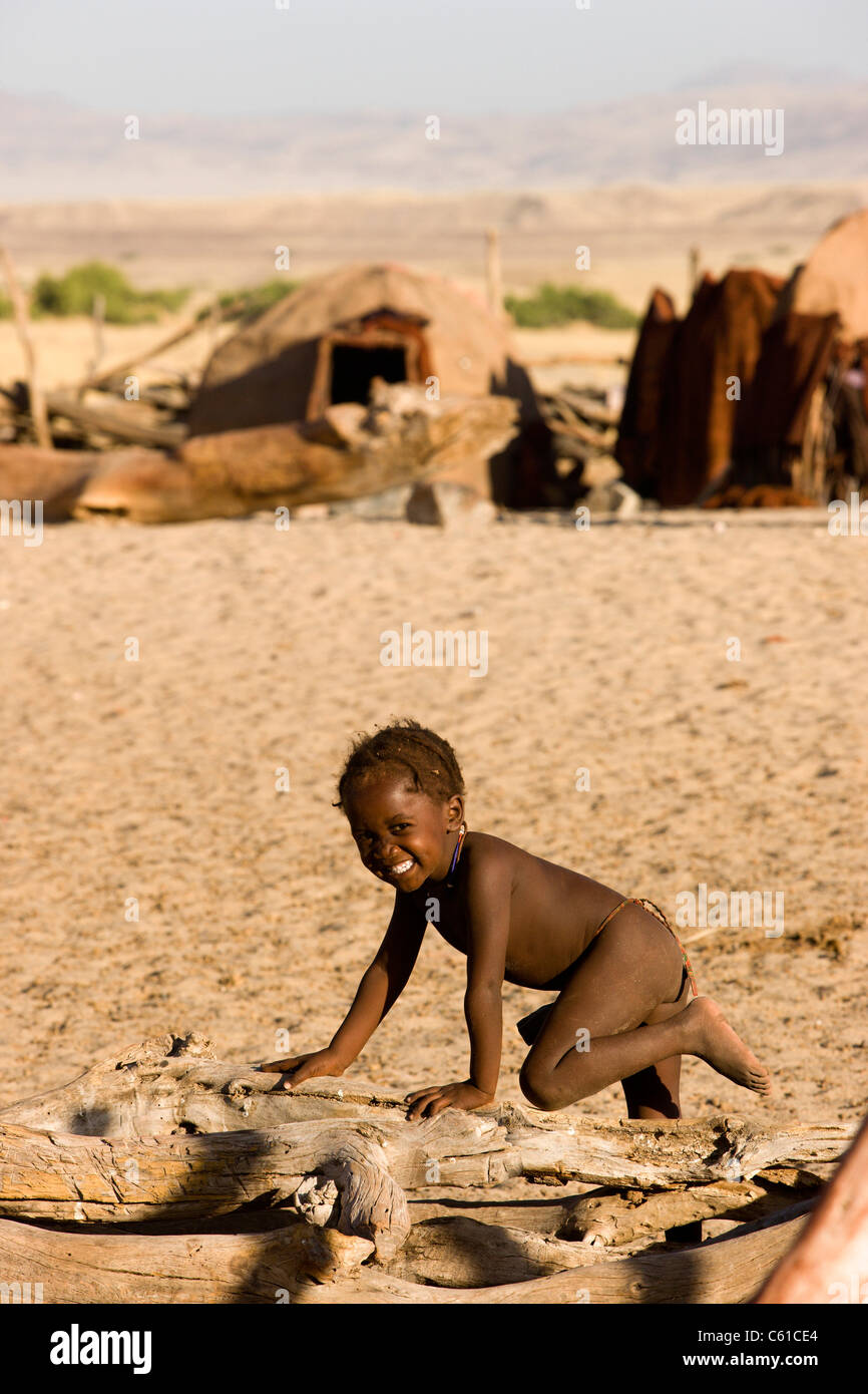Un piccolo felice Himba boy sorrisi mentre si gioca su una parete in legno. Purros, Northern Kaokoland, Kaokoveld, Namibia. Foto Stock