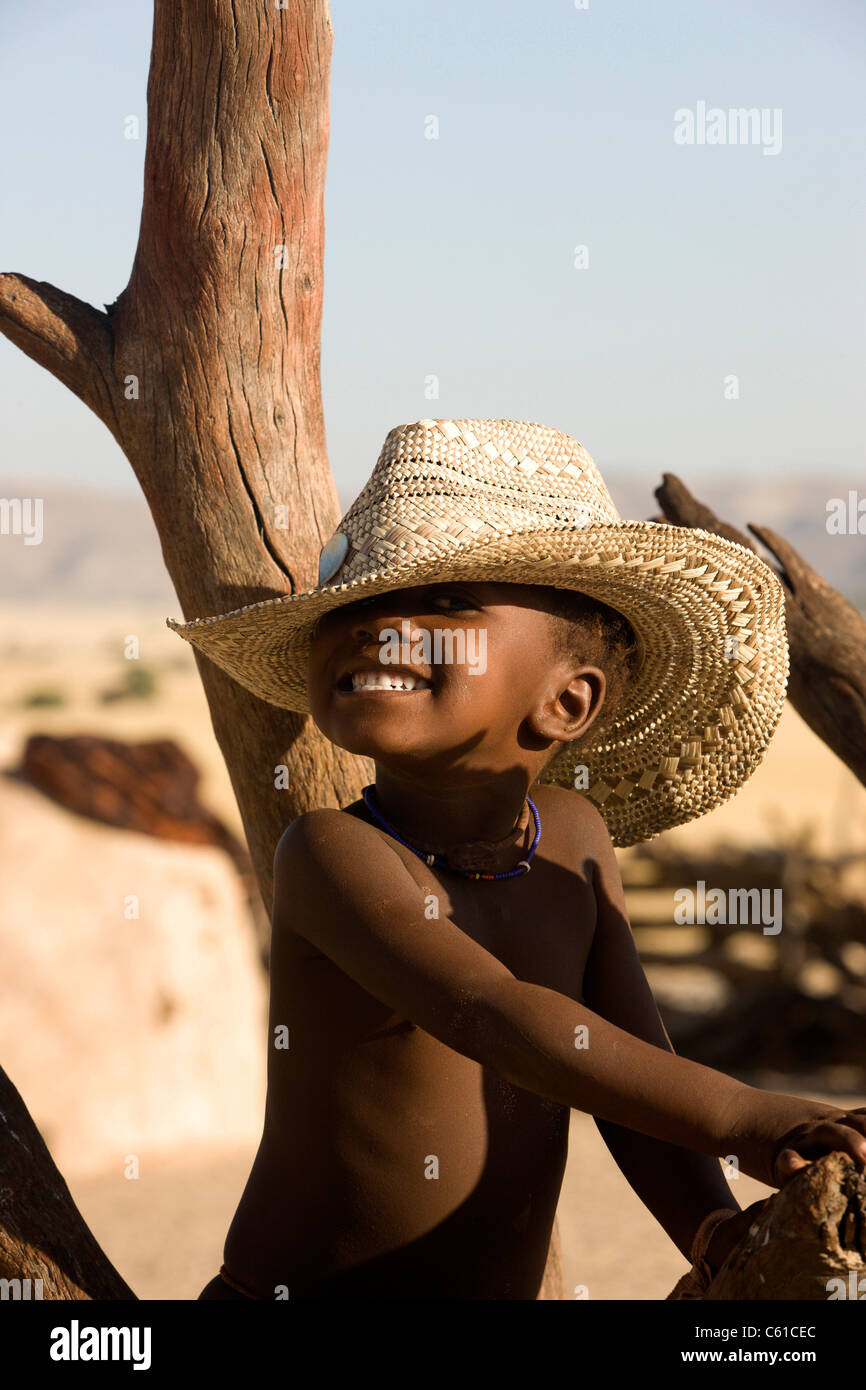 Un piccolo felice Himba boy sorrisi mentre sporting uno stile occidentale hat. Purros, Northern Kaokoland, Kaokoveld, Namibia. Foto Stock