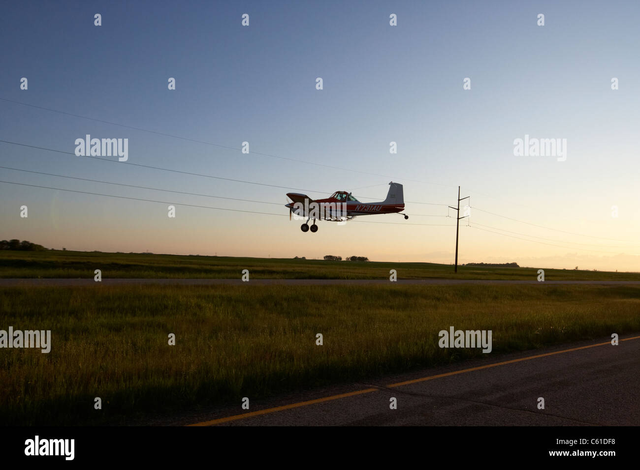 Piccolo cessna un118b cropdusting aerei volando a bassa quota sopra la strada statale e i campi sotto i fili di elettricità il Dakota del Nord Stati Uniti d'America Foto Stock