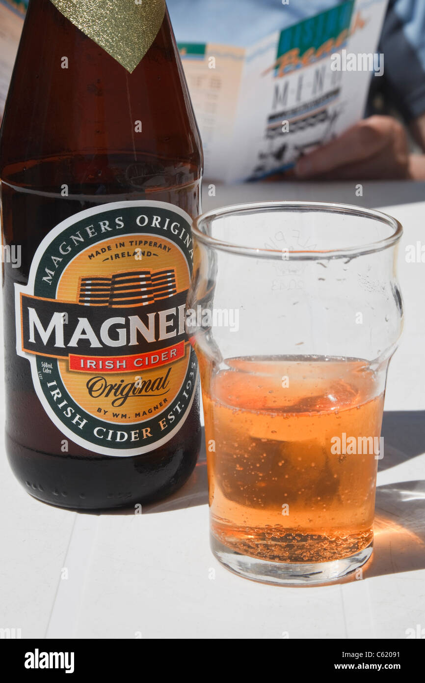 Regno Unito, Gran Bretagna, Europa. Una bottiglia di Magners sidro irlandese con il bicchiere mezzo pieno del bere sulla tavola imbandita di un ristorante all'aperto. Foto Stock
