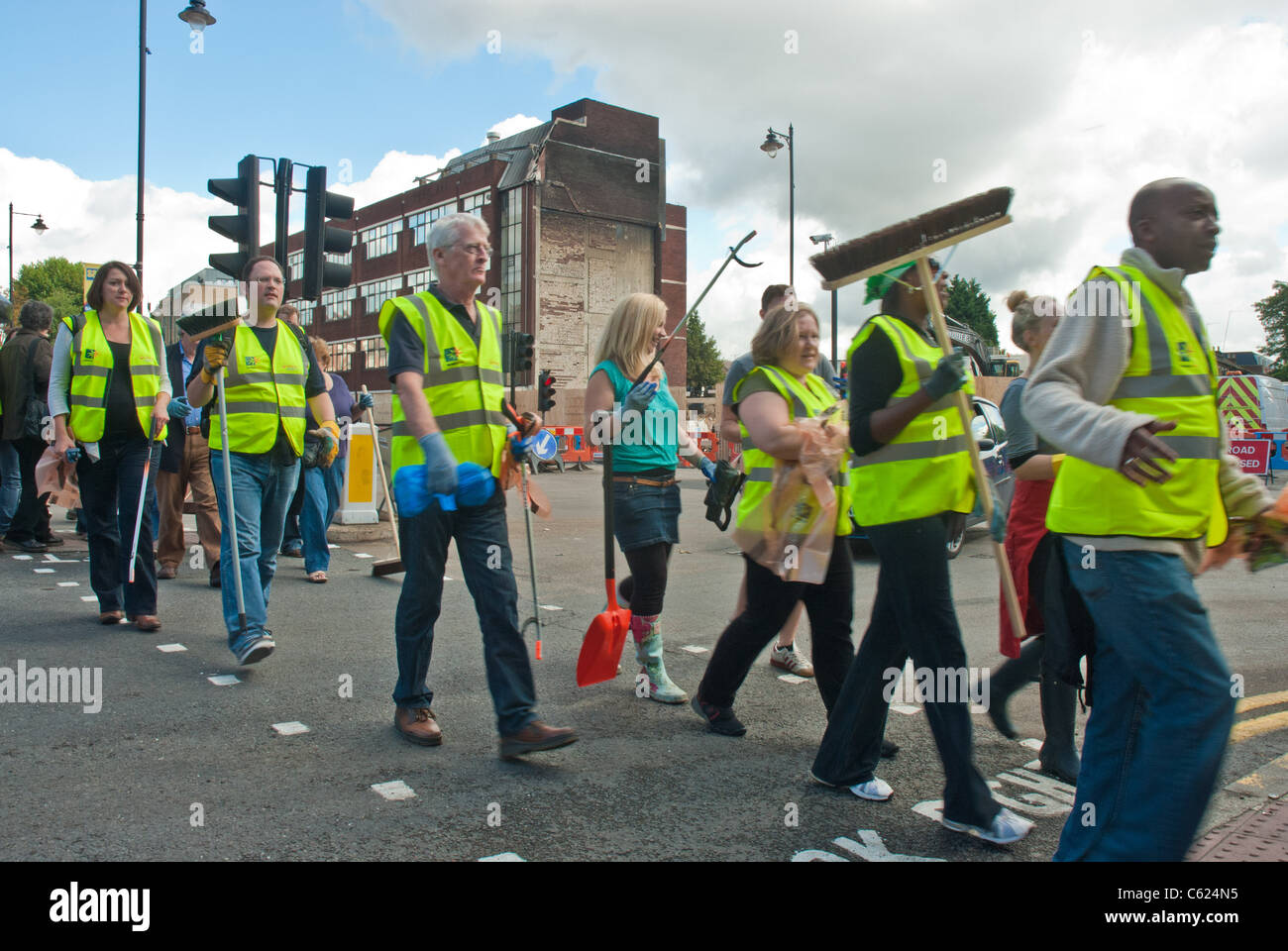 Un gruppo di persone locali compresi i consiglieri che arrivano a pulire dopo Tottenham sommosse con edificio carbonizzati in background Foto Stock