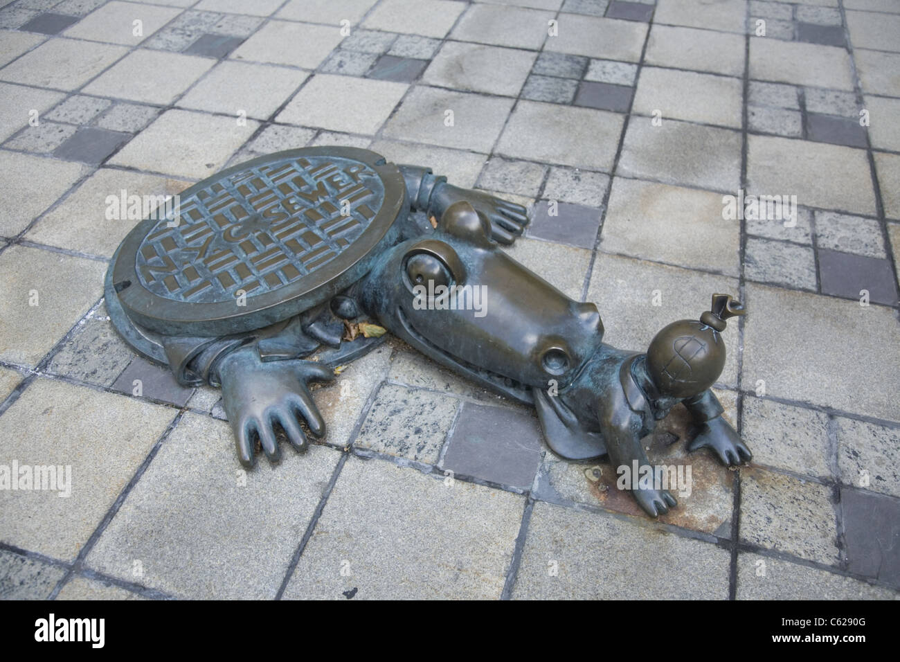 Questi sardonica sculture raffigurano un alligatore emergente da un tombino a mordere in giù su un uomo con un simbolo del dollaro sulla sua testa Foto Stock