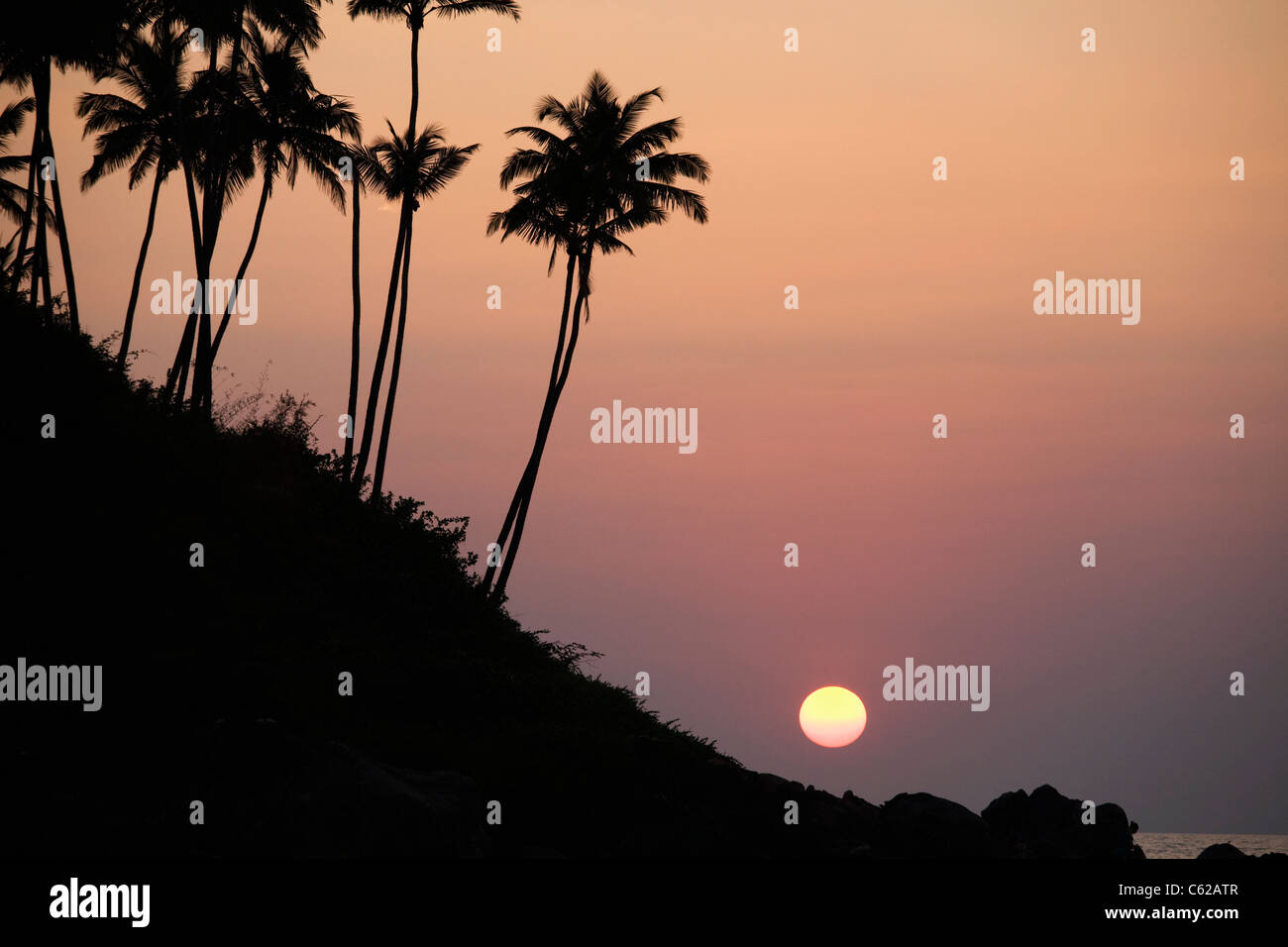 Un sole tropicale imposta nell'oceano stagliano da palme Foto Stock