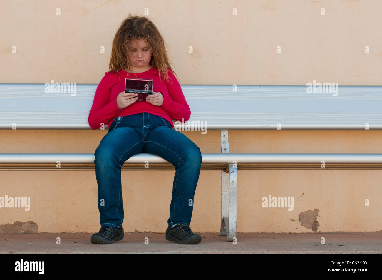 Ragazza adolescente che gioca al vecchio gioco digitale Nintendo sulla panchina Foto Stock