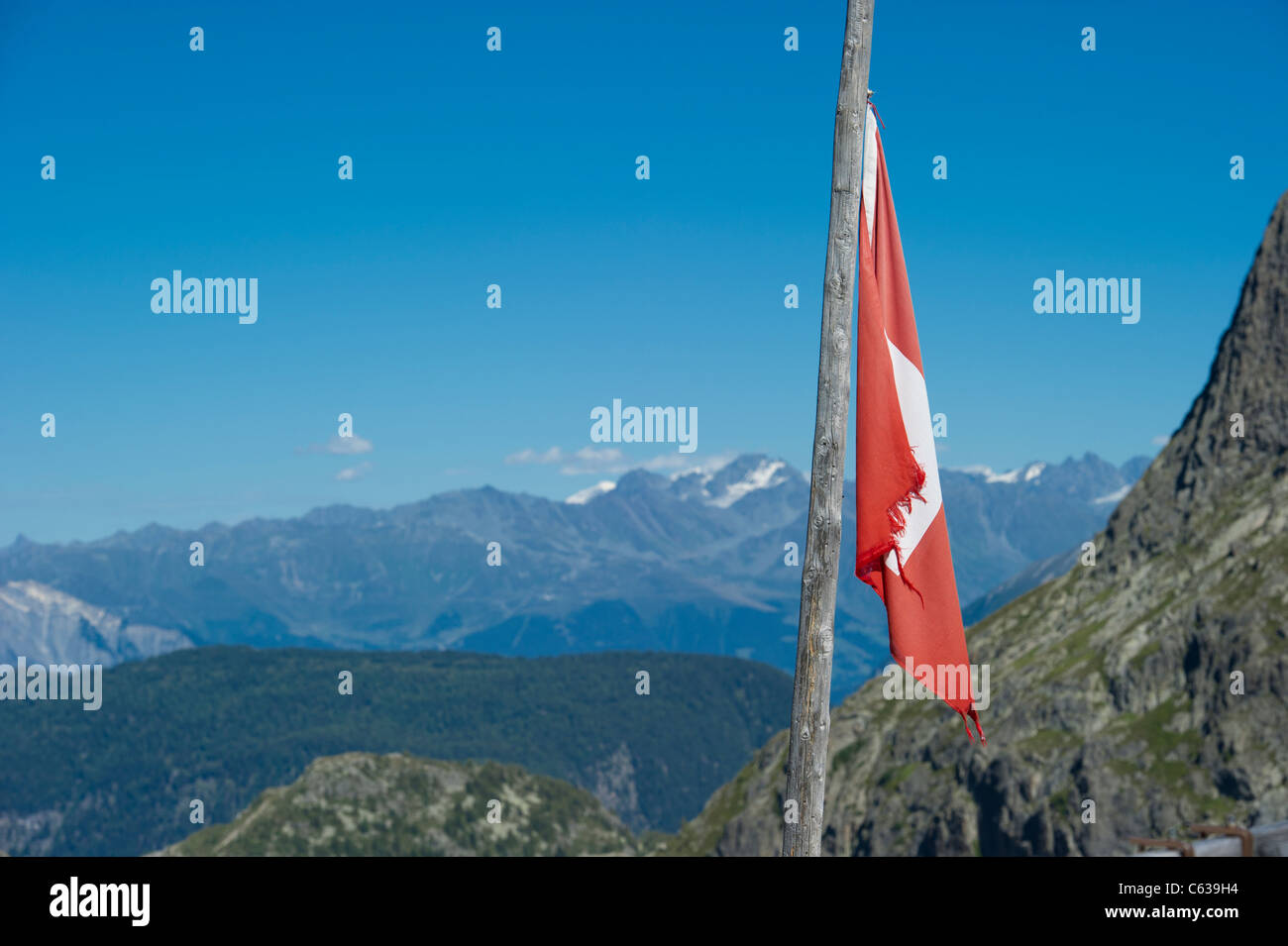 Un weathered swiss bandiera nazionale sul palo ad un rifugio di montagna sopra la diga di Emosson in Vallese, Svizzera. Foto Stock