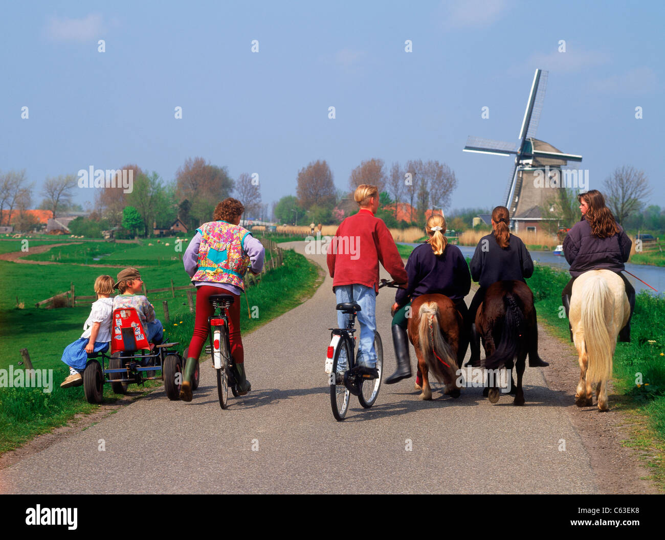 Equitazione per bambini di carretti e pony e biciclette sul rurale elevata canal road in Olanda ultimi mulini a vento e fattorie Foto Stock