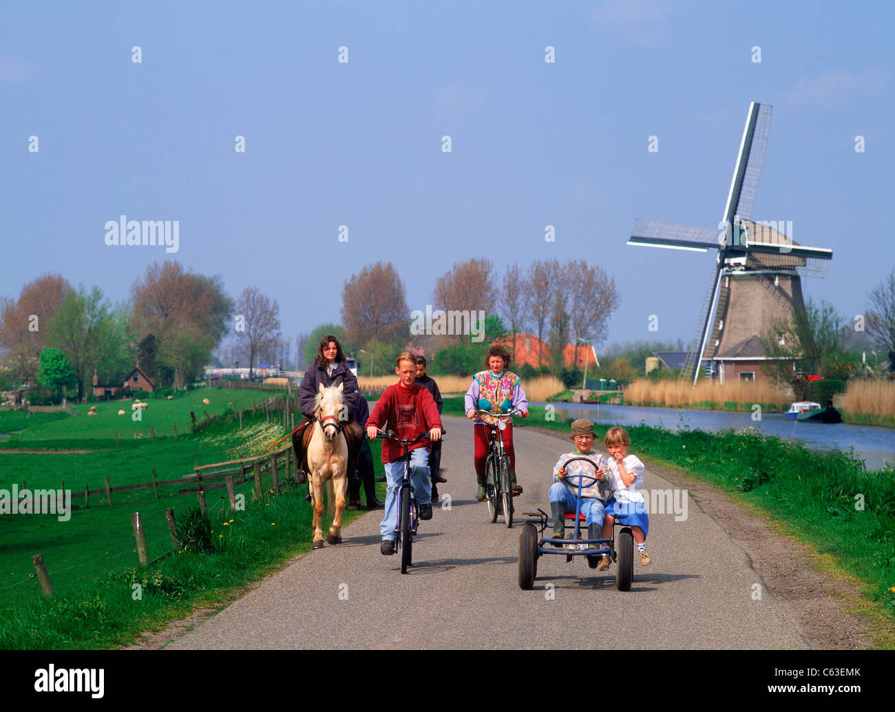 Equitazione per bambini di carretti e pony e biciclette sul rurale elevata canal road in Olanda ultimi mulini a vento e fattorie Foto Stock