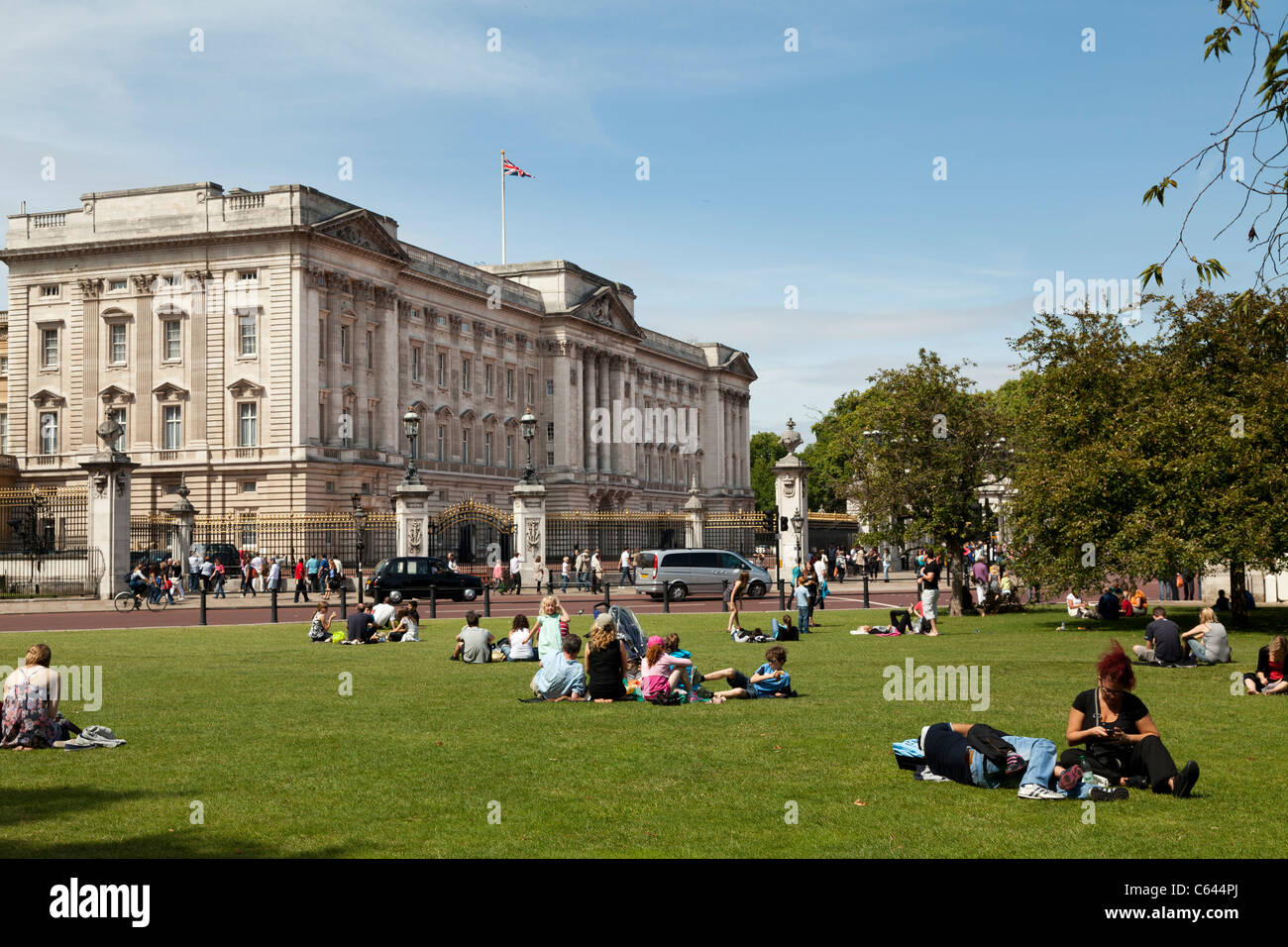 I turisti in appoggio sul prato fuori Buckingham Palace Foto Stock