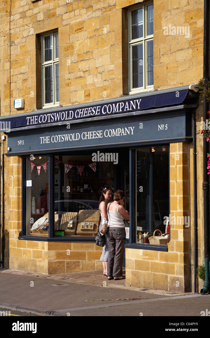 Due donne che guardano nelle finestre del negozio della Cotswold Cheese Company ad High Street, Moreton in Marsh nel Cotswolds, Gloucestershire, Regno Unito nel mese di luglio Foto Stock