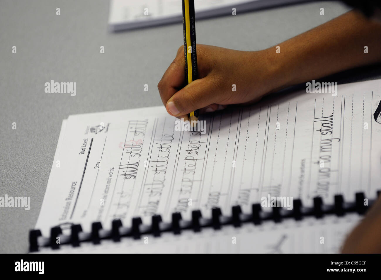 Afro-caraibica studente di scuola di canto la pratica di scrittura in inglese di base con matita su carta rigata Foto Stock