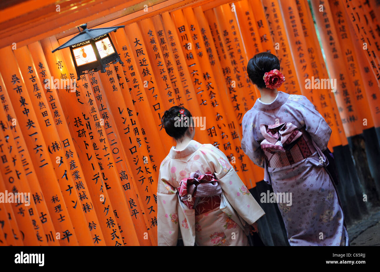 Due donne giapponesi indossando kimono a piedi passato torii o cancelli rossi, fodera un percorso a Fushimi Inari santuario vicino a Kyoto. Foto Stock