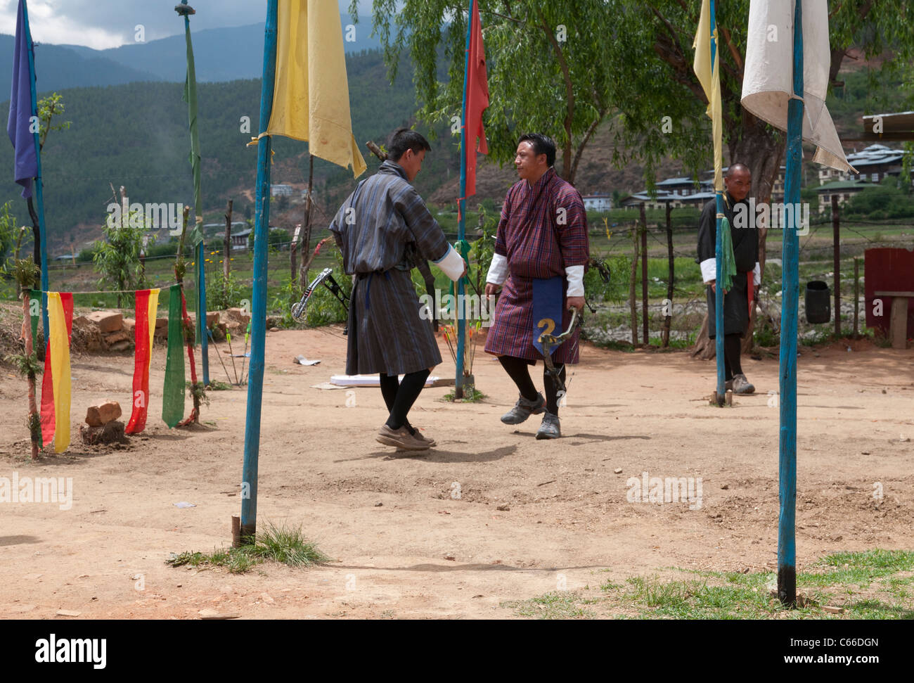 2 Gli uomini in tradizionale gho eseguendo la vittoria danza. paro e tiro con l'arco di massa. Il Bhutan Foto Stock