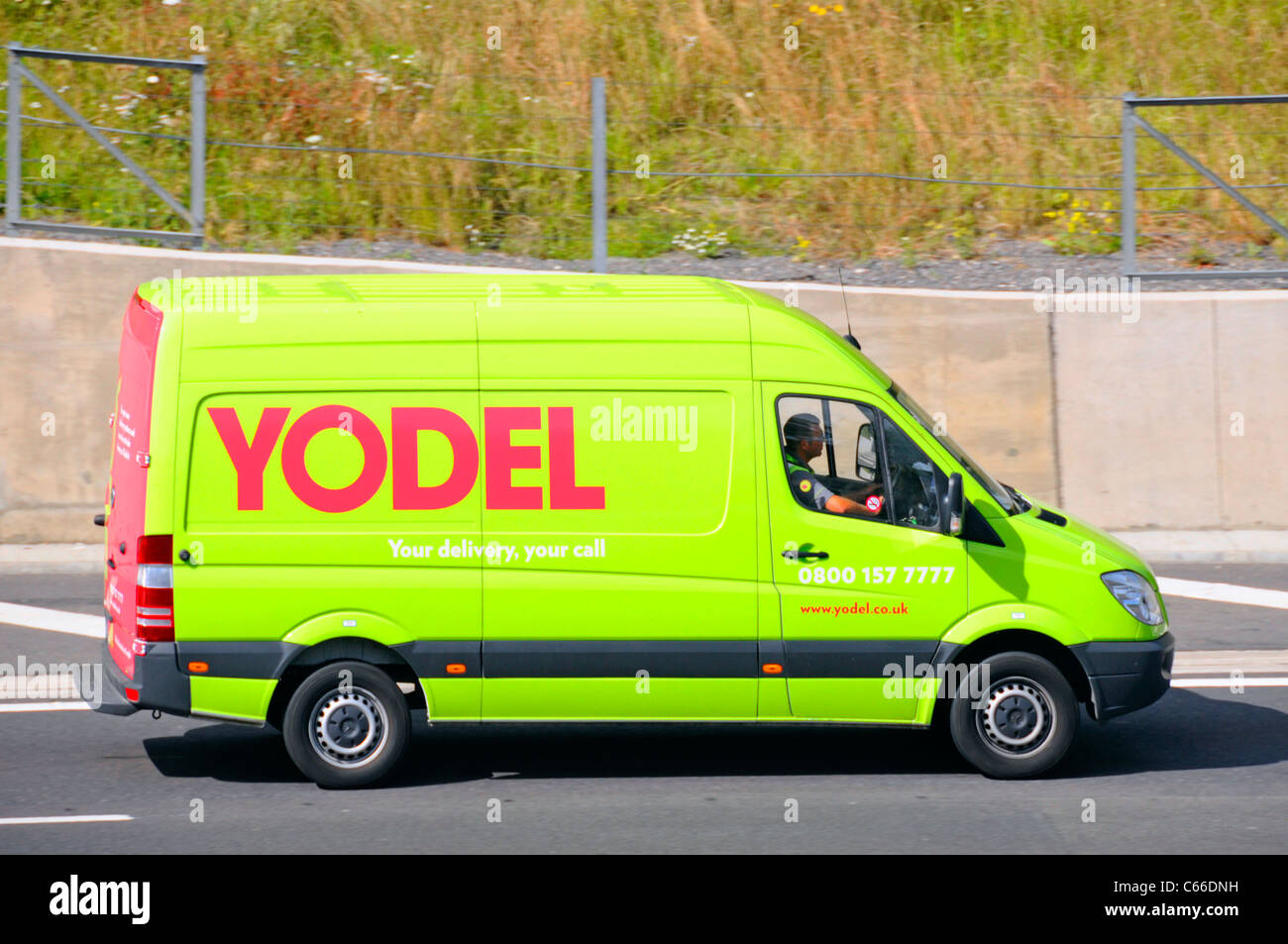Vista laterale Yodel logistica trasporto furgone di consegna e conducente parte Del commercio nazionale di consegna dei pacchi della catena di fornitura che guida lungo il Regno Unito autostrada Foto Stock