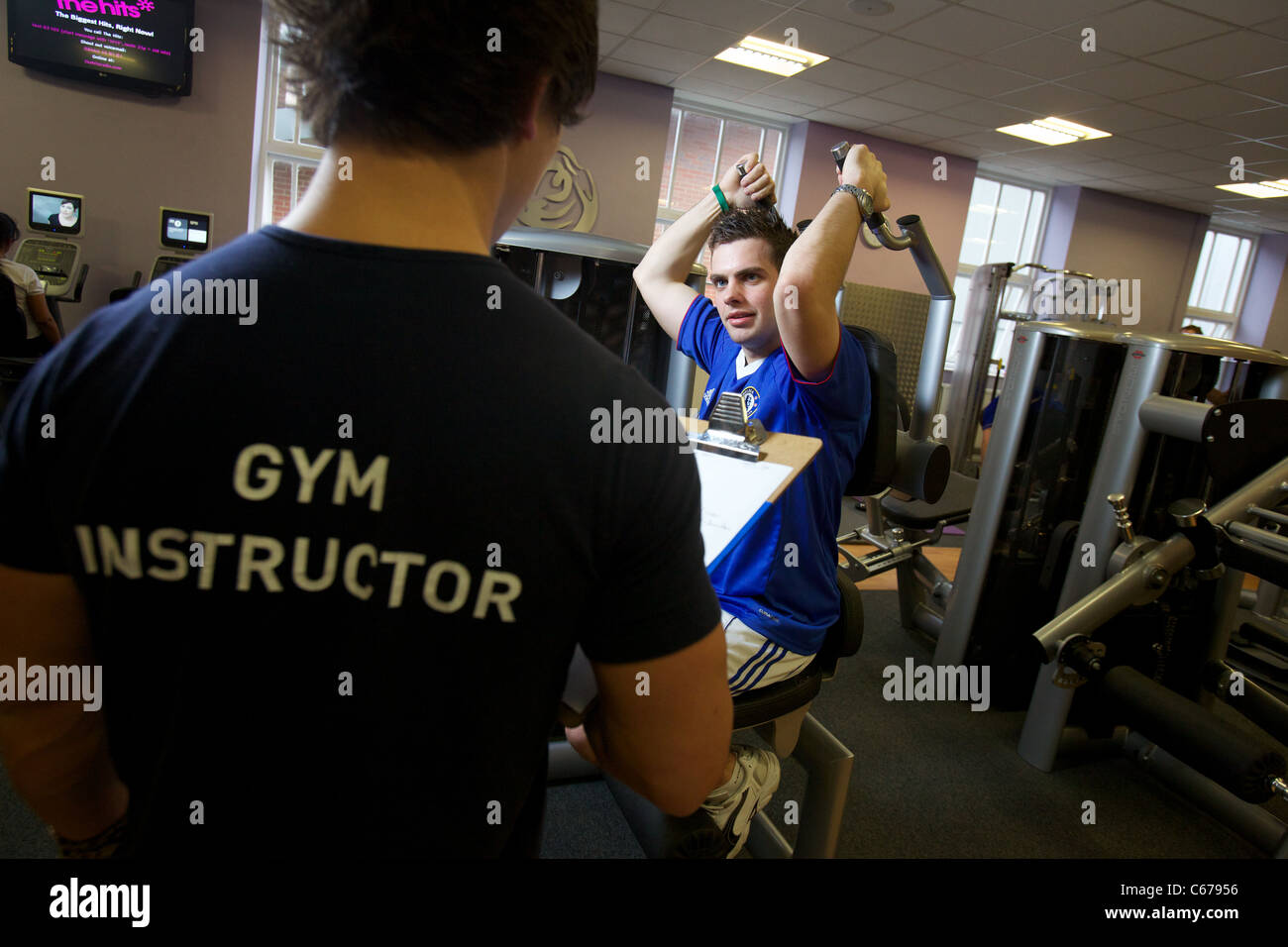 Istruttore di palestra conducendo una palestra valutazione su un corpo interno edificio estensione braccio macchina Foto Stock