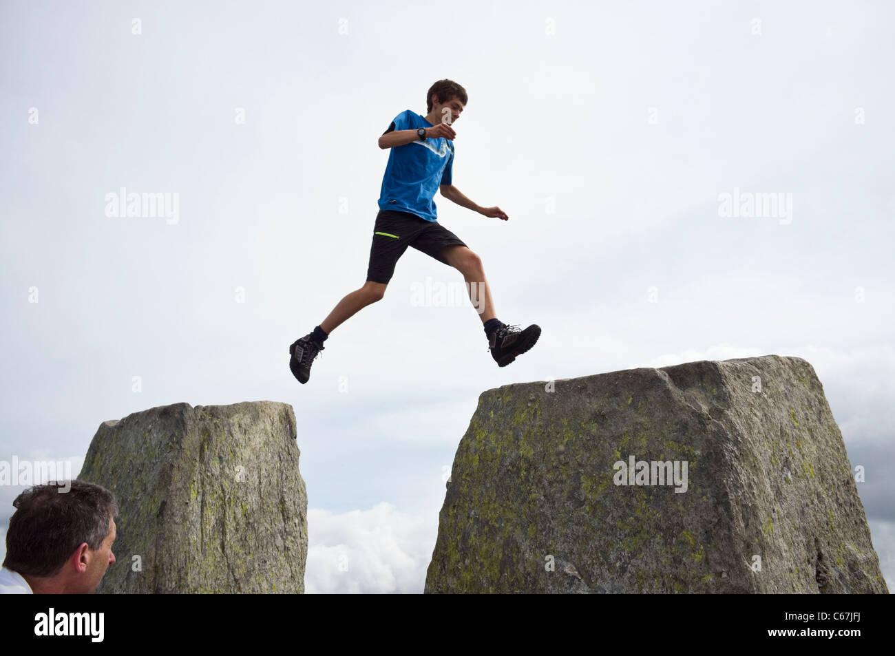 Teenager che salta attraverso il divario tra Adam e Eve pietre sulla cima del Monte Tryfan montagna cima nel Parco Nazionale di Snowdonia Galles del Nord Gran Bretagna Foto Stock