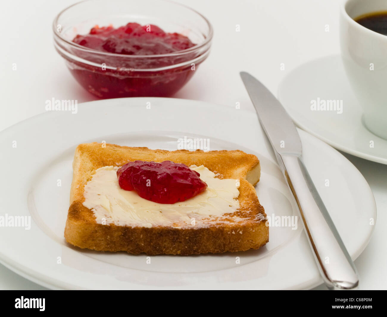 Una piastra withe una fetta di pane tostato e una piccola ciotola di marmellata, accanto è una tazza di caffè Foto Stock