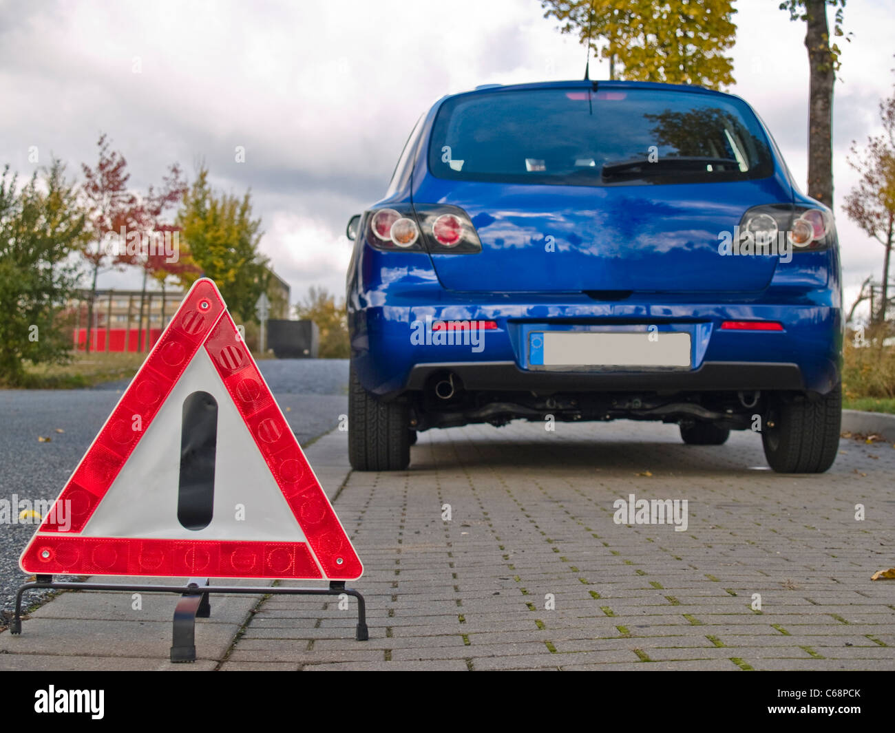 Ein Warndreieck, davor steht ein blaues Auto | un triangolo di avvertenza, davanti è un auto blu Foto Stock