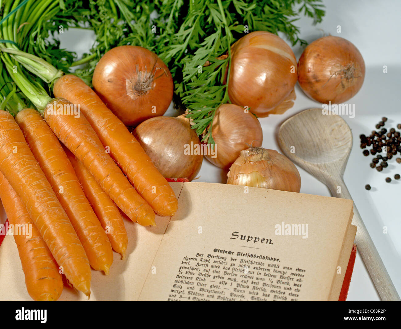Un vecchio libro di cucina tedesca a fianco a fianco con le carote, cipolle e grani di pepe e un cucchiaio di legno Foto Stock