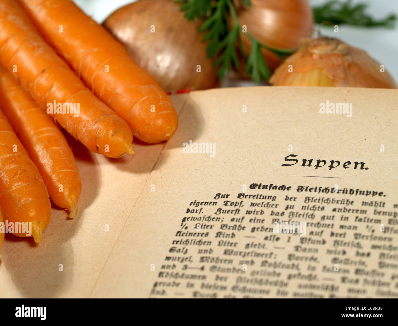 Un vecchio libro di cucina tedesca a fianco di carote e cipolle Foto Stock