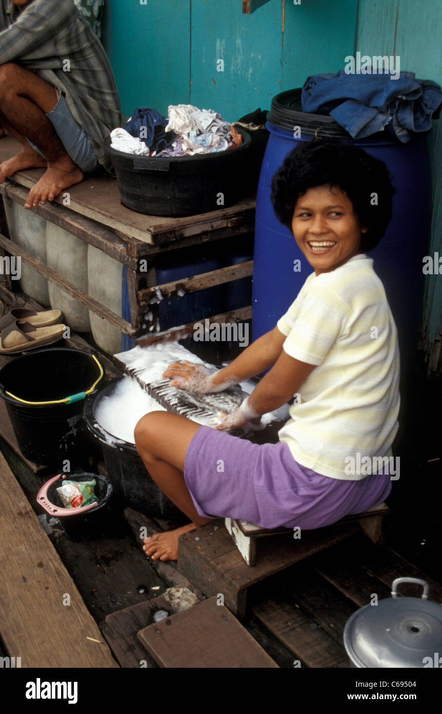 Donna sorridente facendo il bucato nell'Pasar Ikan baraccopoli, Jakarta, Indonesia Foto Stock