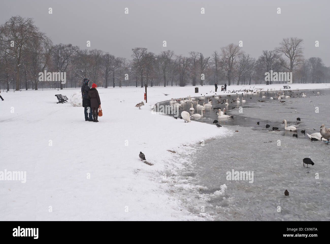 L'Hyde Park di Londra in inverno dopo la nevicata con un paio in piedi accanto a uccelli alimentazione allo stagno rotondo Foto Stock
