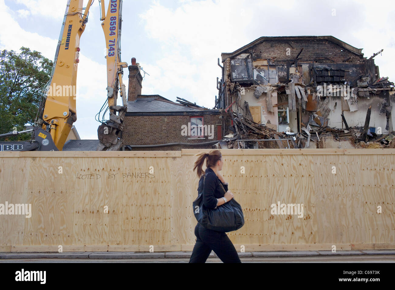 Un ben vestiti donna con una coda di cavallo cammina davanti a un edificio su Tottenham High Road bruciate in Londra summer tumulti. Foto Stock