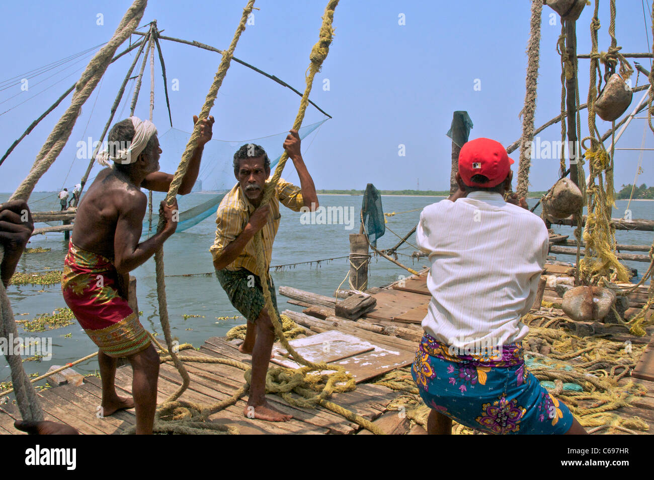 I pescatori cinese di funzionamento delle reti da pesca Fort Cochin Kerala India del Sud Foto Stock