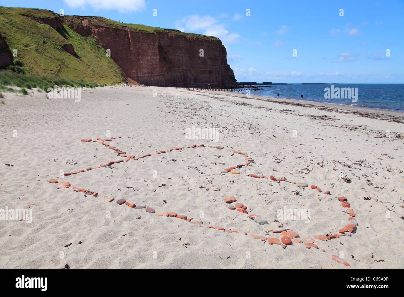 Cupido dart attraverso il cuore è fatta di pietre presso la spiaggia Nord su isola di Helgoland, Germania; Nordstrand auf Helgoland Foto Stock