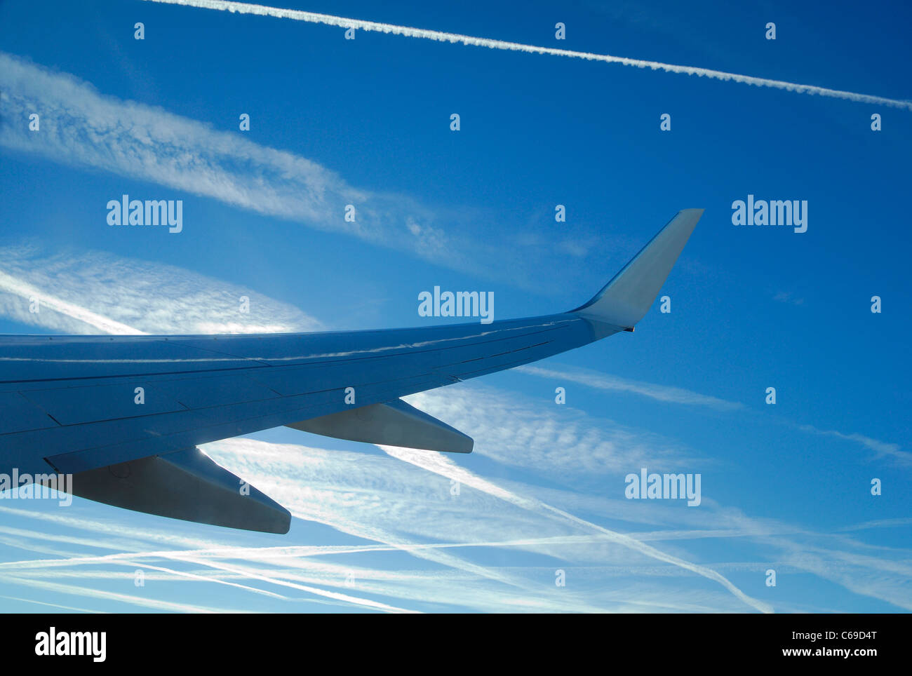 Ala di aereo di linea su un cielo blu pieno di piani di scarico tracce generando cirrus nuvole (Ci) formarsi durante l'inverno, Francia Foto Stock