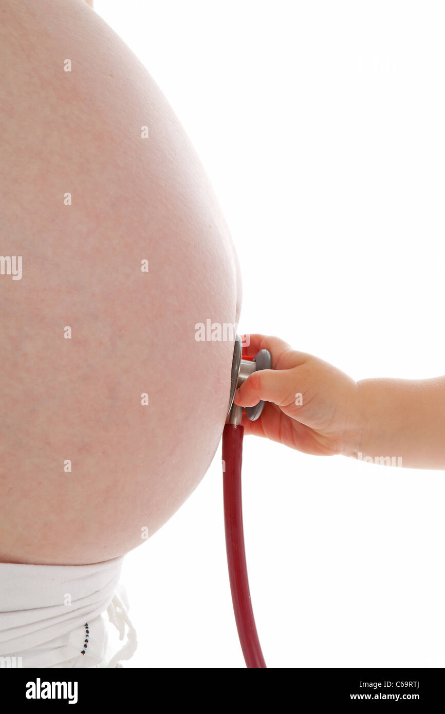 I bambini la mano con uno stetoscopio sul ventre in gravidanza in primo piano su sfondo bianco Foto Stock