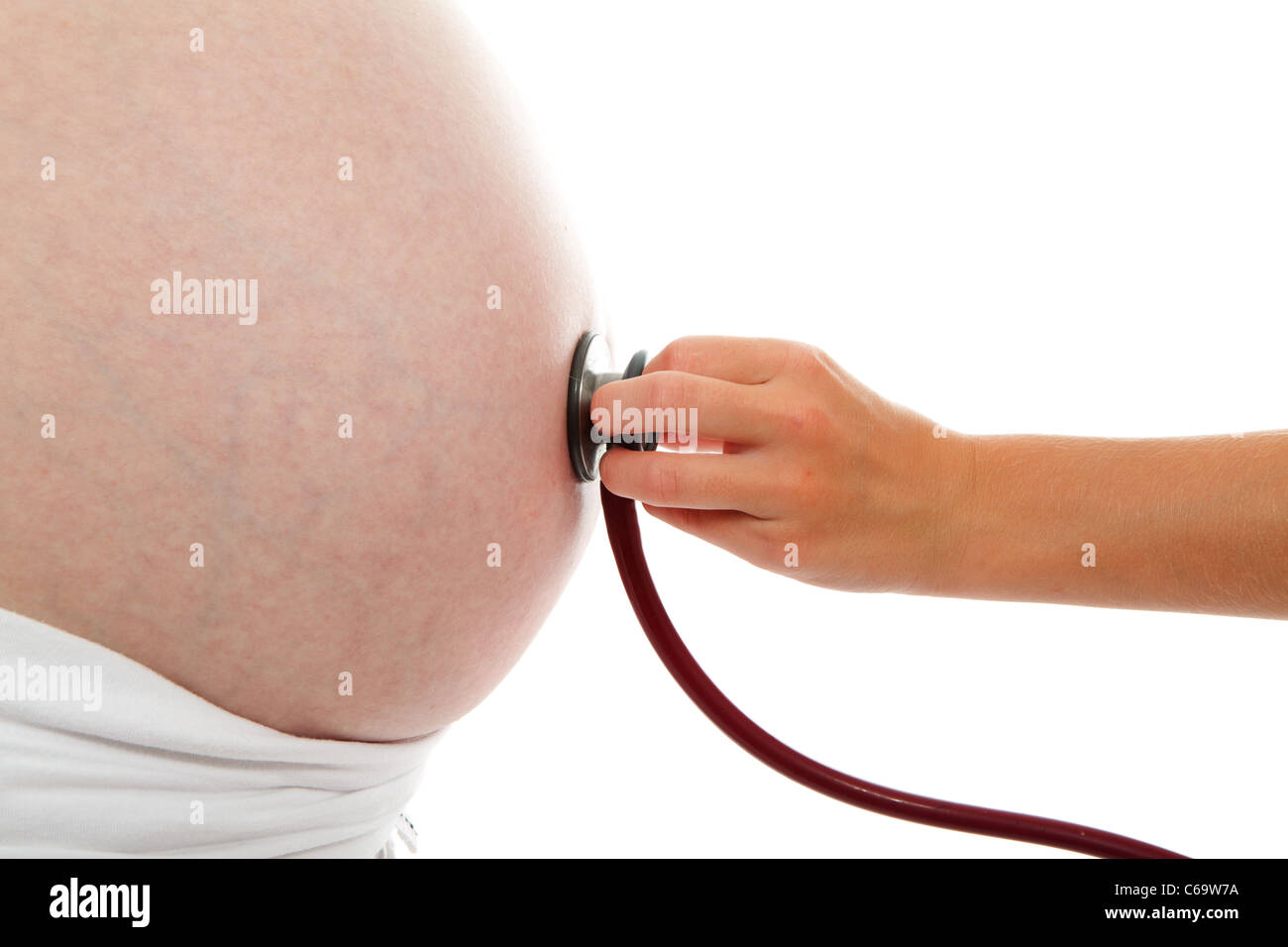 Childs mano con uno stetoscopio sul ventre in gravidanza su sfondo bianco Foto Stock