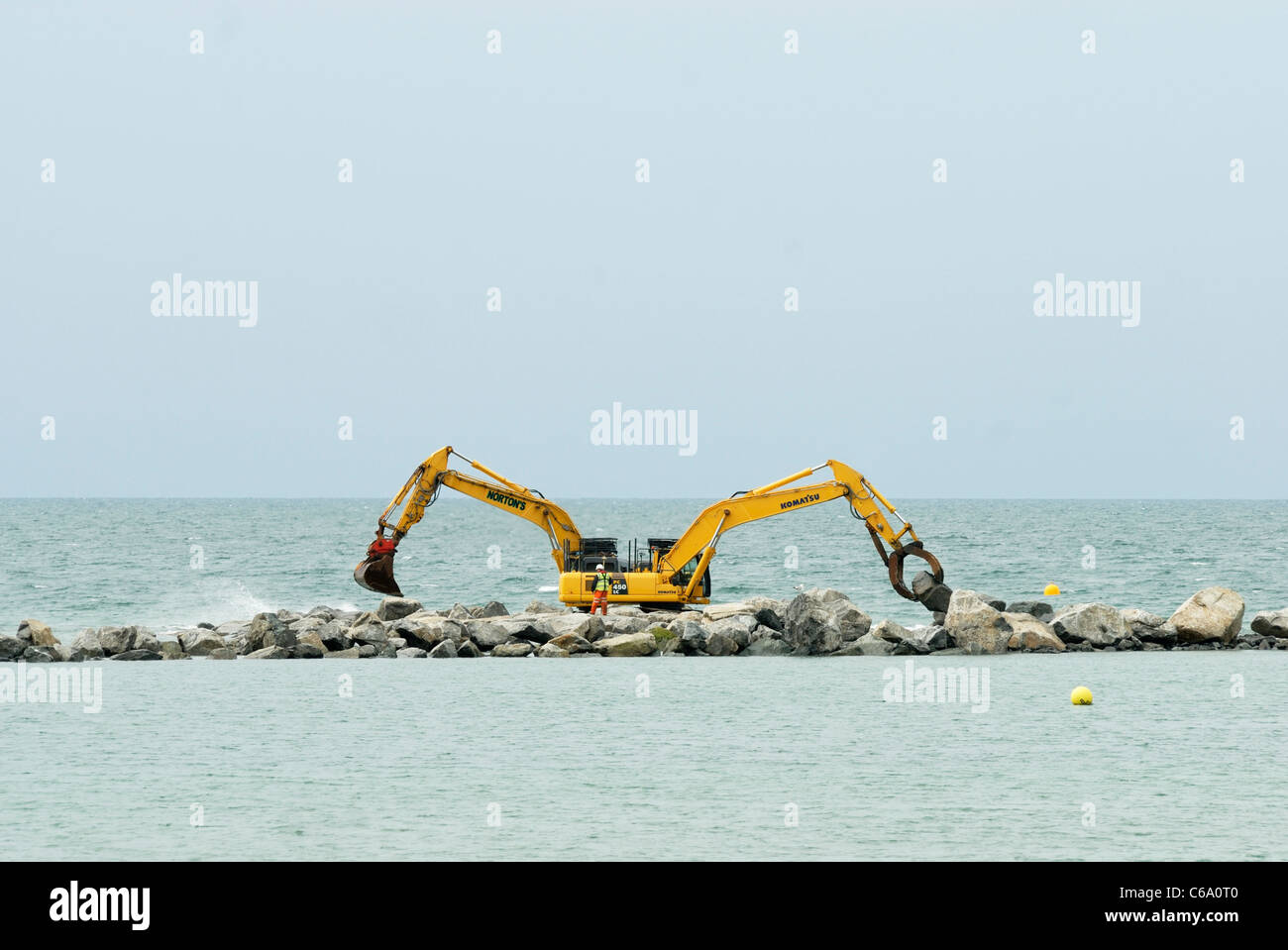Una coppia di macchine di scavo la costruzione di un reef artificiale, parte delle difese del mare per il villaggio di Borth, Ceredigion, Galles Foto Stock
