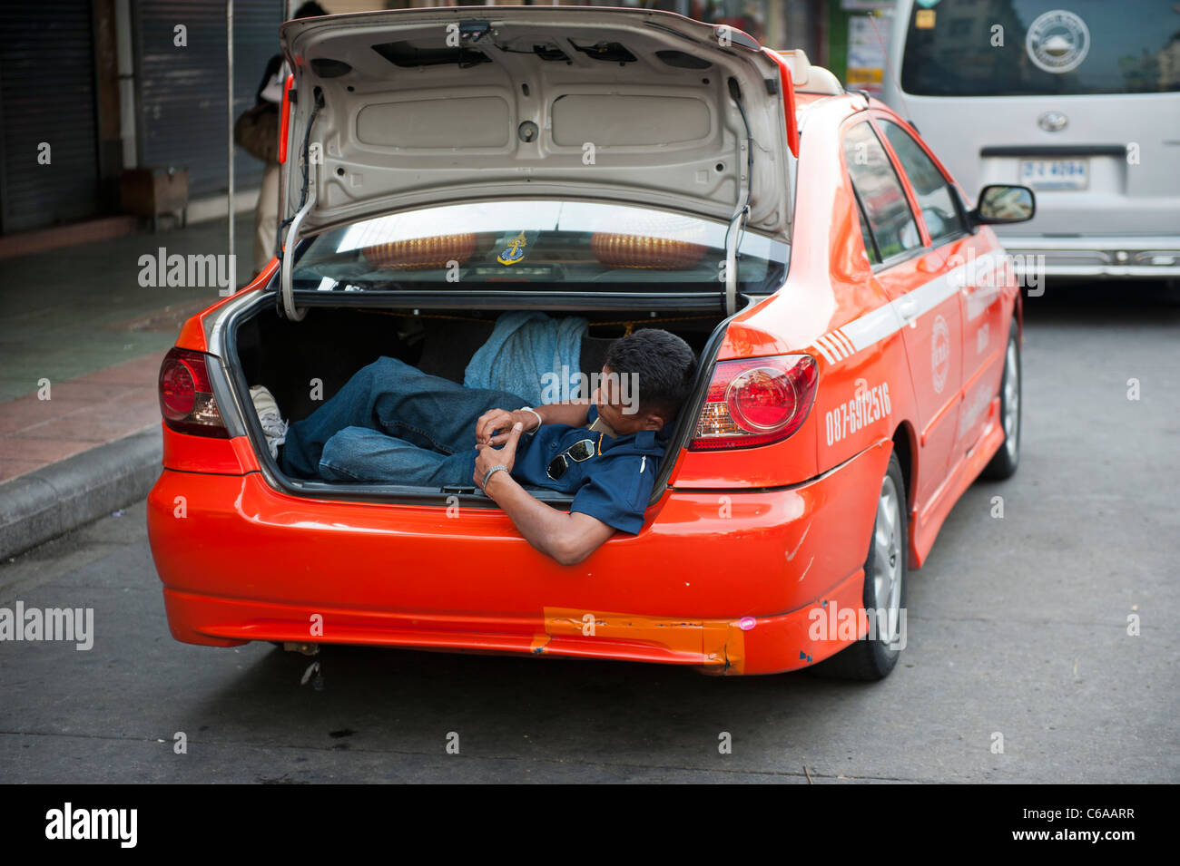 Un maschio di Bangkok taxi driver prendendo un pisolino nel bagagliaio della sua cabina rosso. Della Thailandia Foto Stock