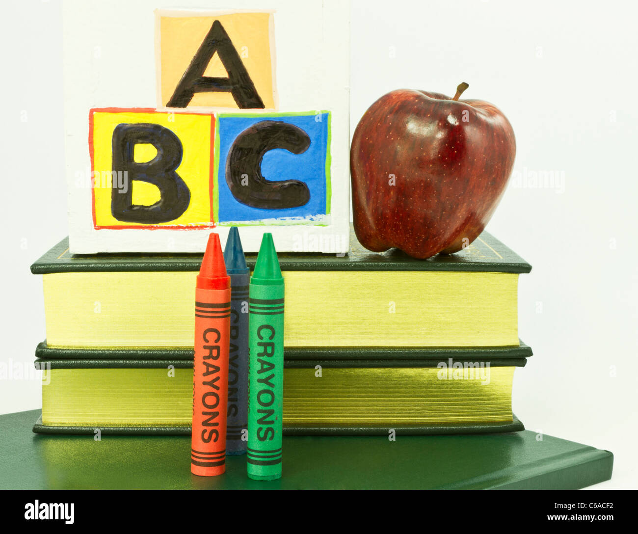 Tre matite colorate, ABC blocchi, apple rosso posto su libri su sfondo bianco. Foto Stock