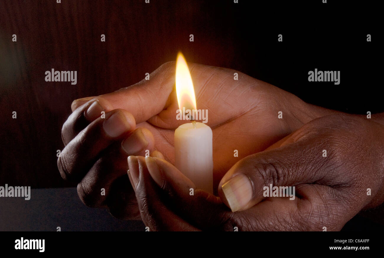 African la mano che regge un cero acceso dando calore, sicurezza e luce. studio shot su sfondo scuro; Foto Stock